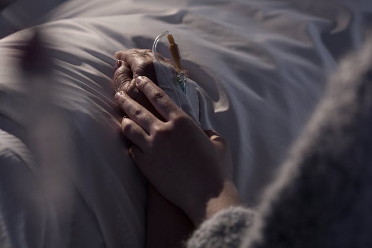 One hand holds another on a hospital bed.
